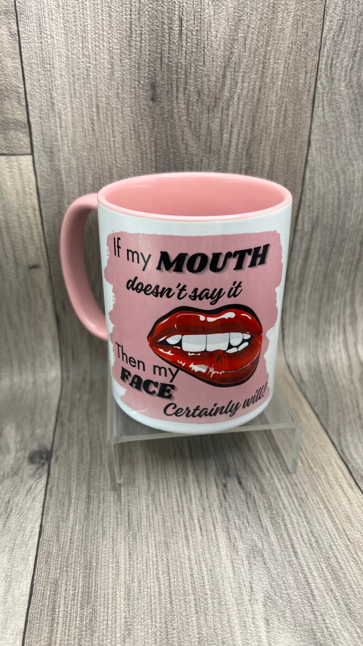A white ceramic mug with pink interior and pink handle. The mug design features bold red lips and white teeth and the text reads: "If my MOUTH doesn't say it, then my FACE certainly will" in black and grey lettering.