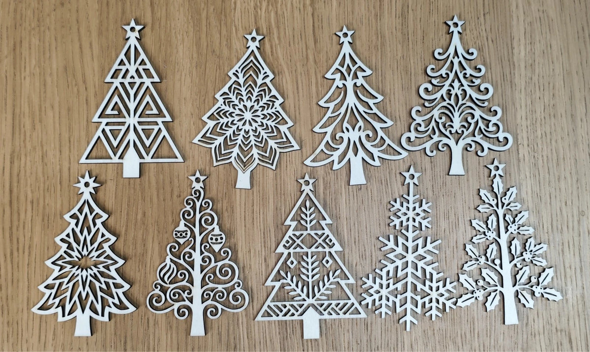 Nine white laser-cut wooden Christmas tree ornaments in various intricate patterns, arranged on a light brown wood grain background.