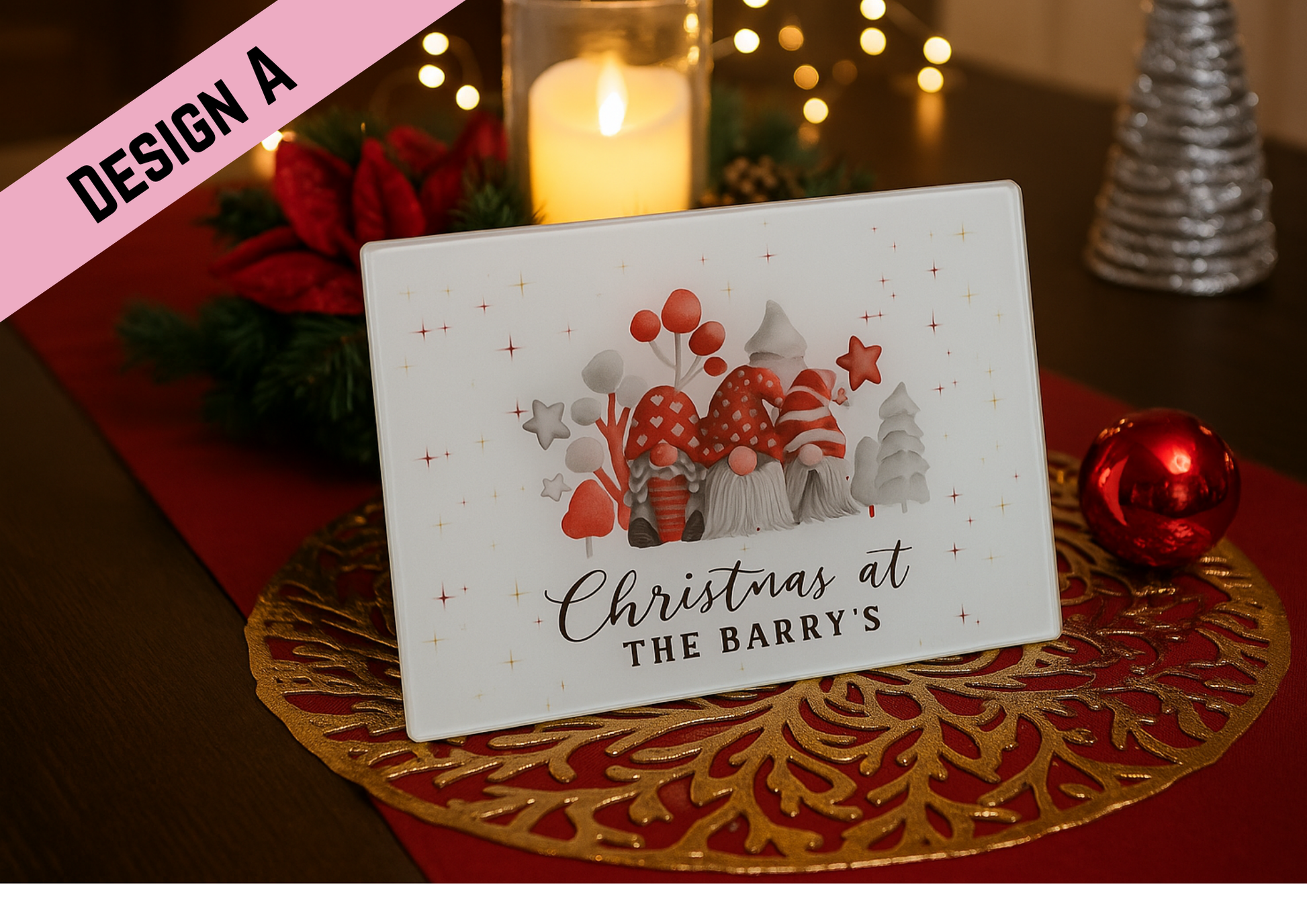 A festive glass placemat reading “Christmas at the Barry’s” with three red-and-white gnomes and Christmas trees in the design, displayed on a tabletop surrounded by warm holiday decorations including candles, a poinsettia, and a gold ornament.