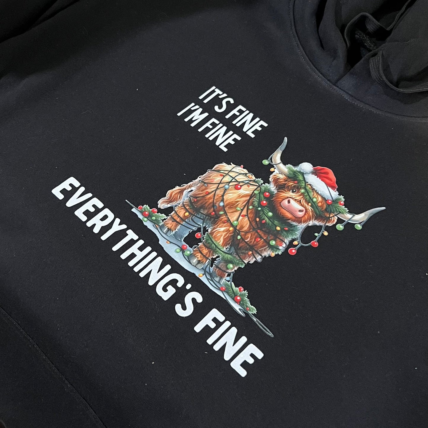 Black hoodie with Festive Highland Cow graphic design reading 'It's Fine, I'm Fine, Everything's Fine'