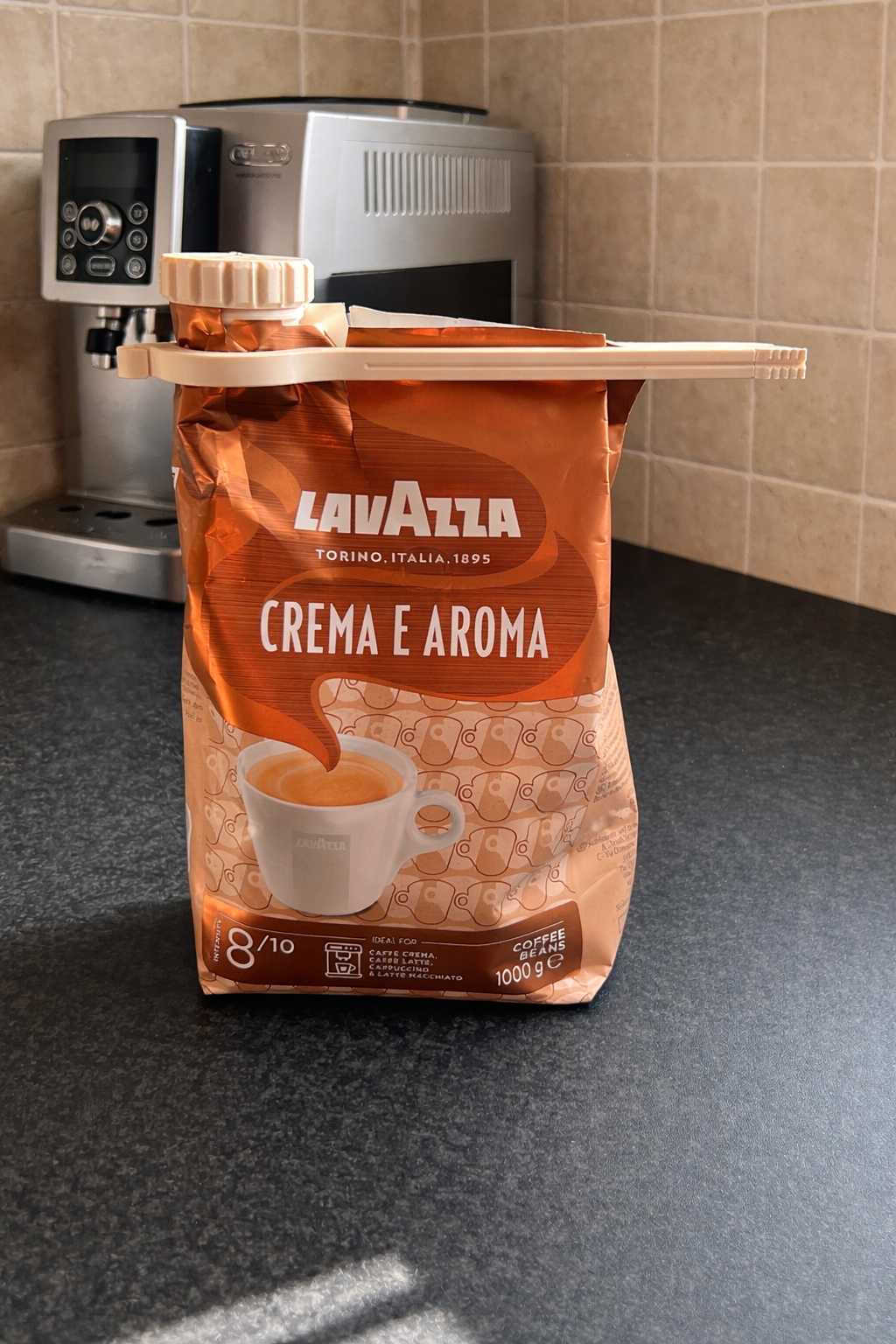 Coffee bag clip sealing a Lavazza Crema e Aroma coffee bean bag on a kitchen countertop with coffee machine in background