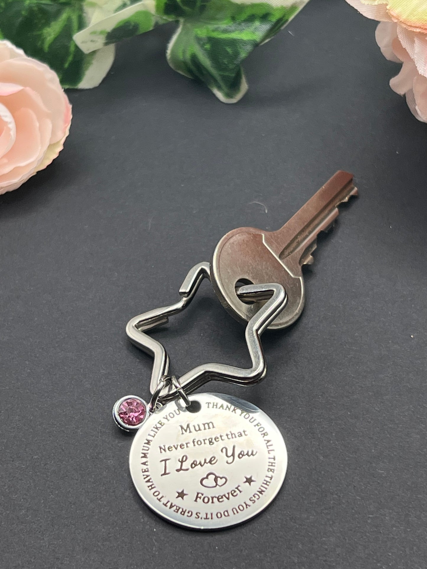 Star shaped key chain with a pink jewel charm and a circle tag charm with the words "Mum Never forget that I Love You Forever" inscribed in the middle.  There is a key attached to the keychain to show its functionality.