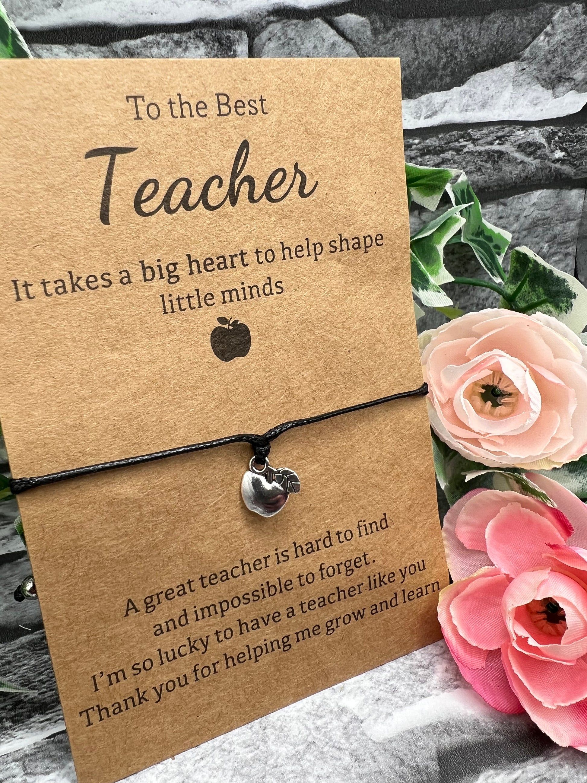 A black 1mm thick waxed cord bracelet with a small silver apple shaped charm in the middle which is wrapped around some brown card reading "To the Best Teacher.  It takes a big heart to help shape little minds.  A great teacher is hard to find and impossible to forget. I'm so lucky to have a teacher like you. Thank you for helping me grow and learn.