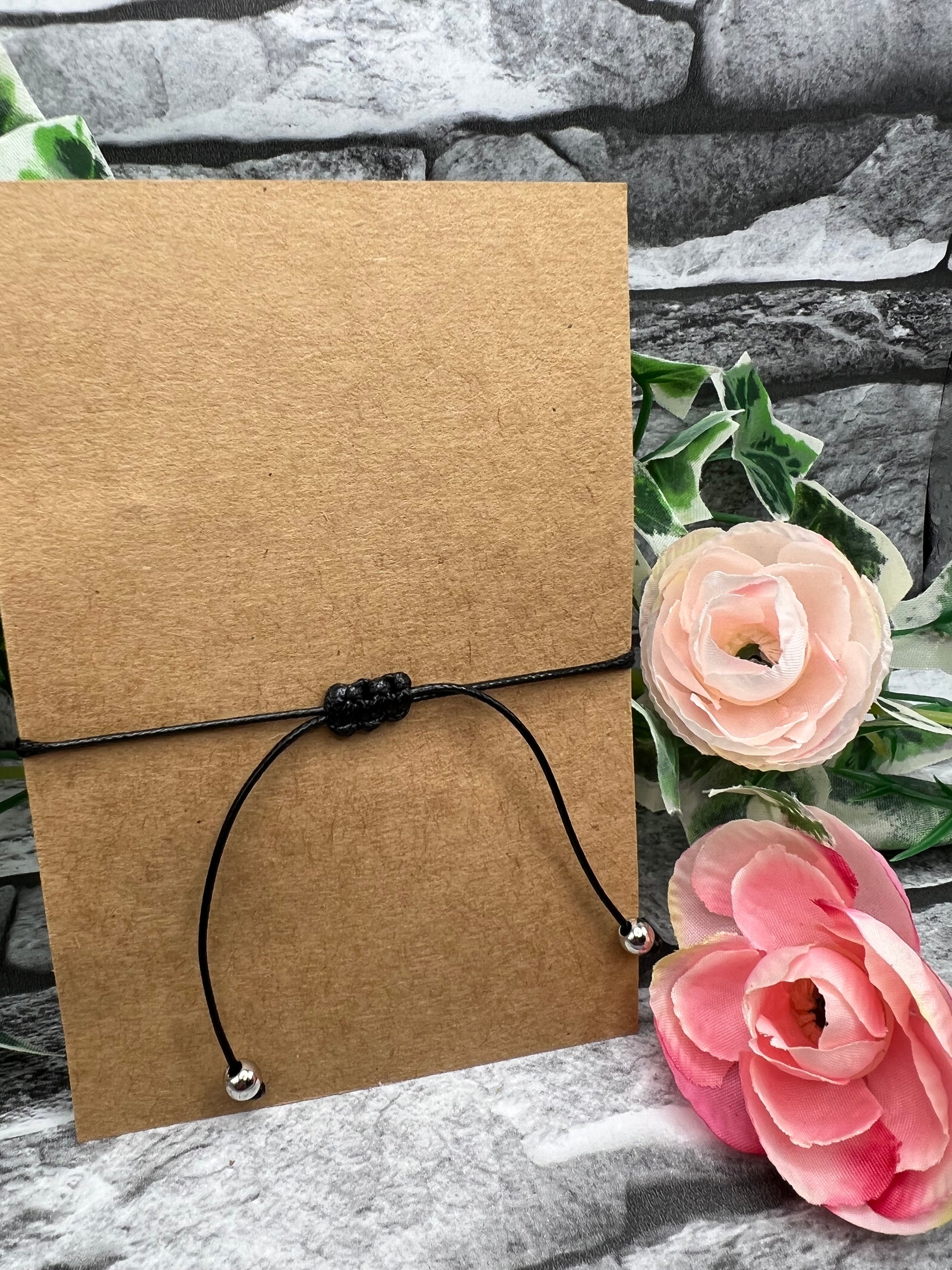 The slip knot used to adjust a black 1mm thick waxed cord bracelet which is wrapped around a piece of brown craft card.