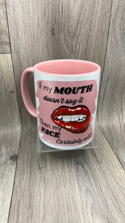 A white ceramic mug with pink interior and pink handle.  The mug design features bold red lips and white teeth and the text reads: "If my MOUTH doesn't say it, then my FACE certainly will" in black and grey lettering.