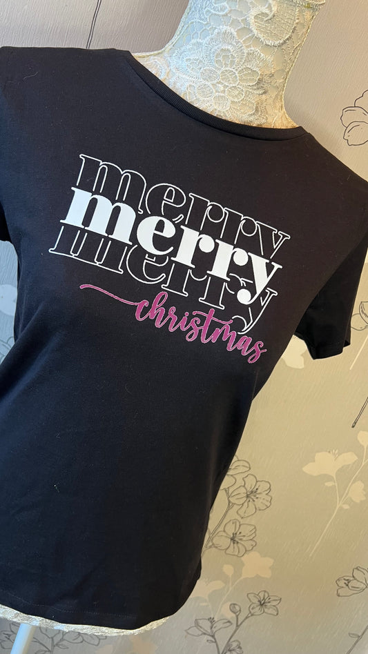 Black t-shirt with 'merry merry christmas' text on a mannequin against a floral-patterned wall.