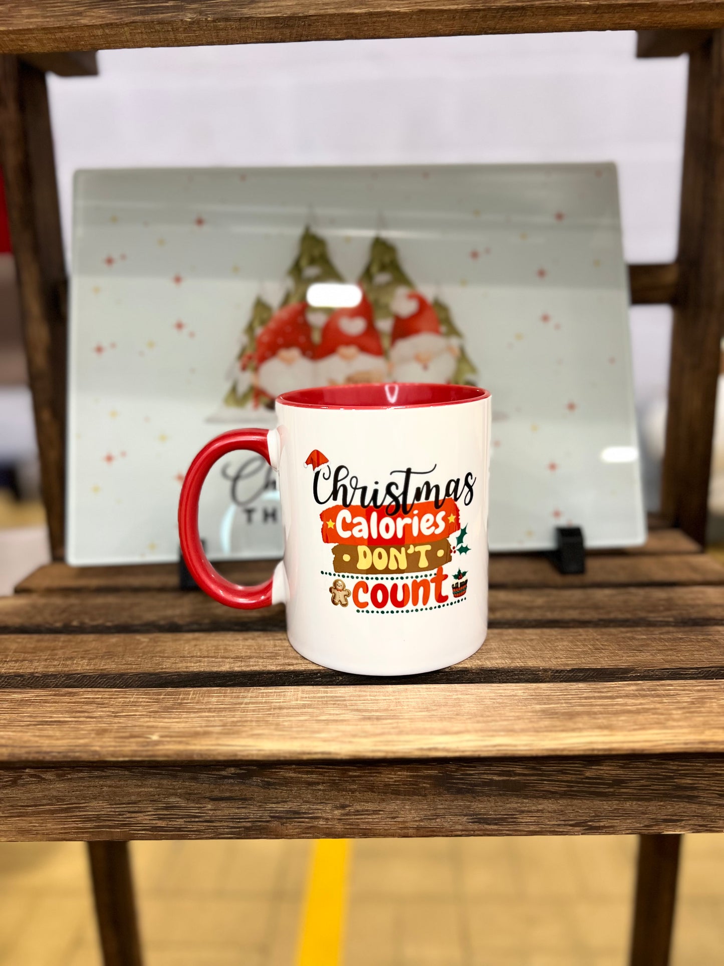 White mug with red handle and interior Christmas theme that reads 'Christmas Calories Don't Count' standing on a wooden surface.