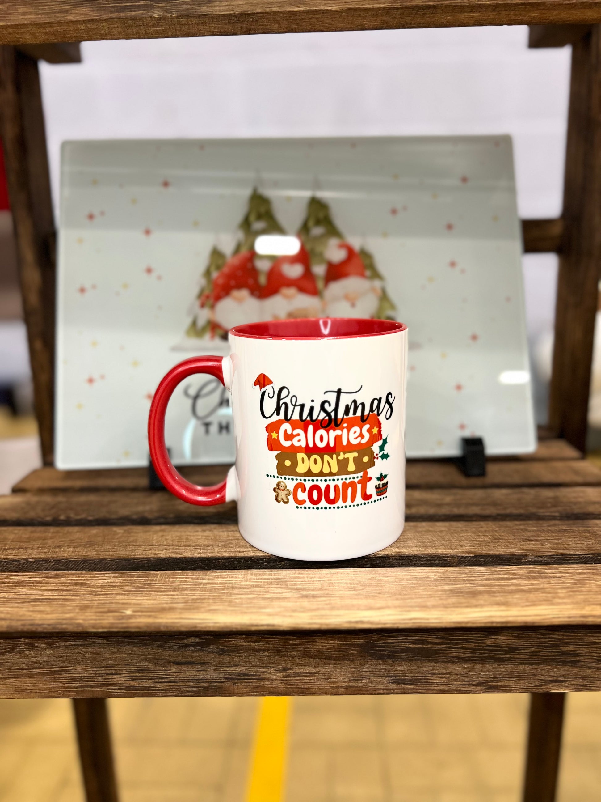 White mug with red handle and interior Christmas theme that reads 'Christmas Calories Don't Count' standing on a wooden surface.
