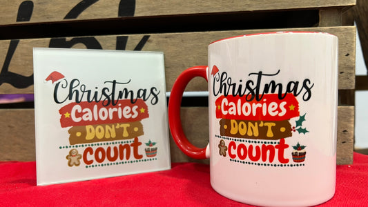 Mug and coaster with 'Christmas Calories Don't Count' text on a red surface.