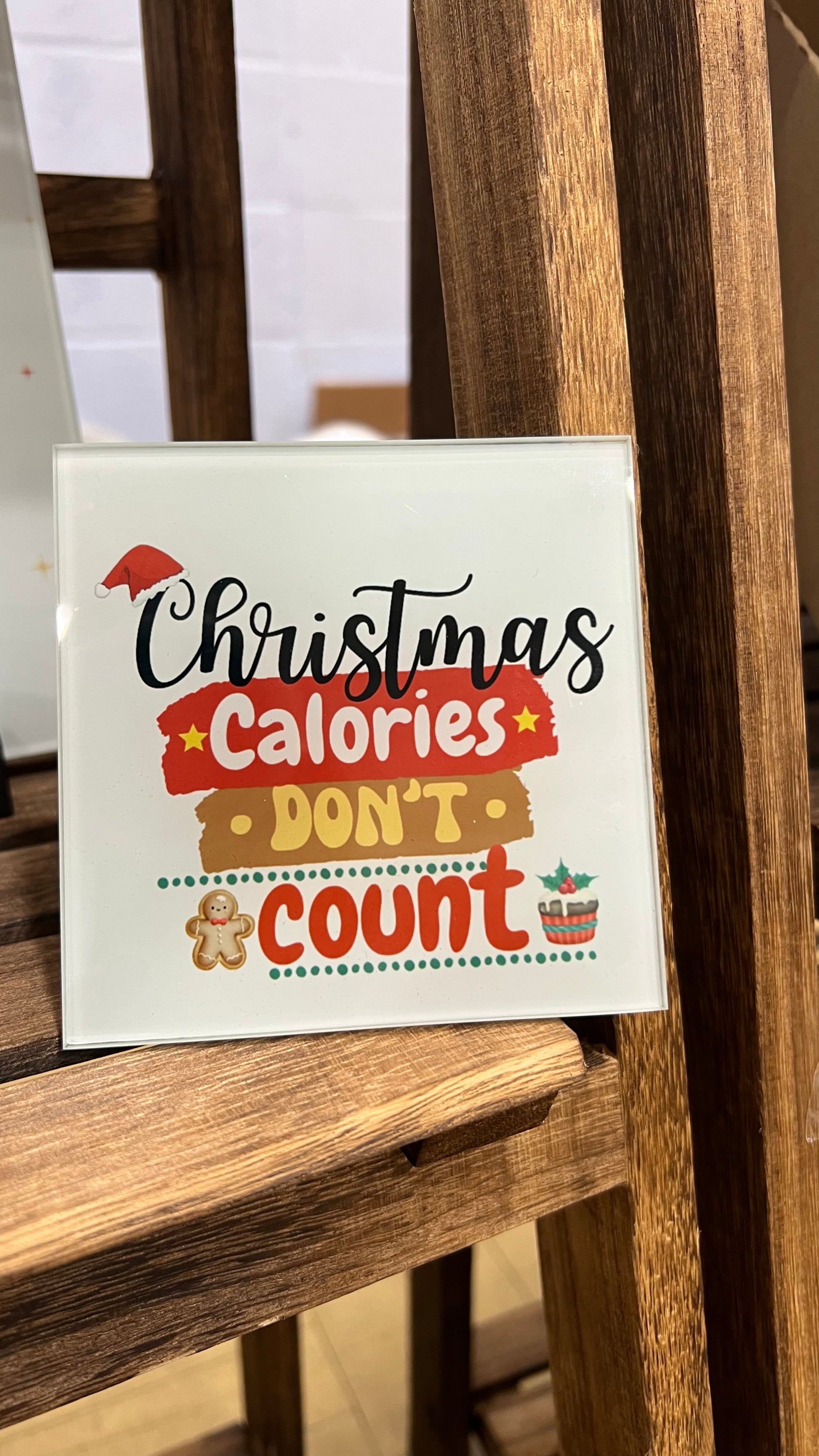 Glass Coaster with 'Christmas Calories Don't Count' text leaning on a wooden shelf.