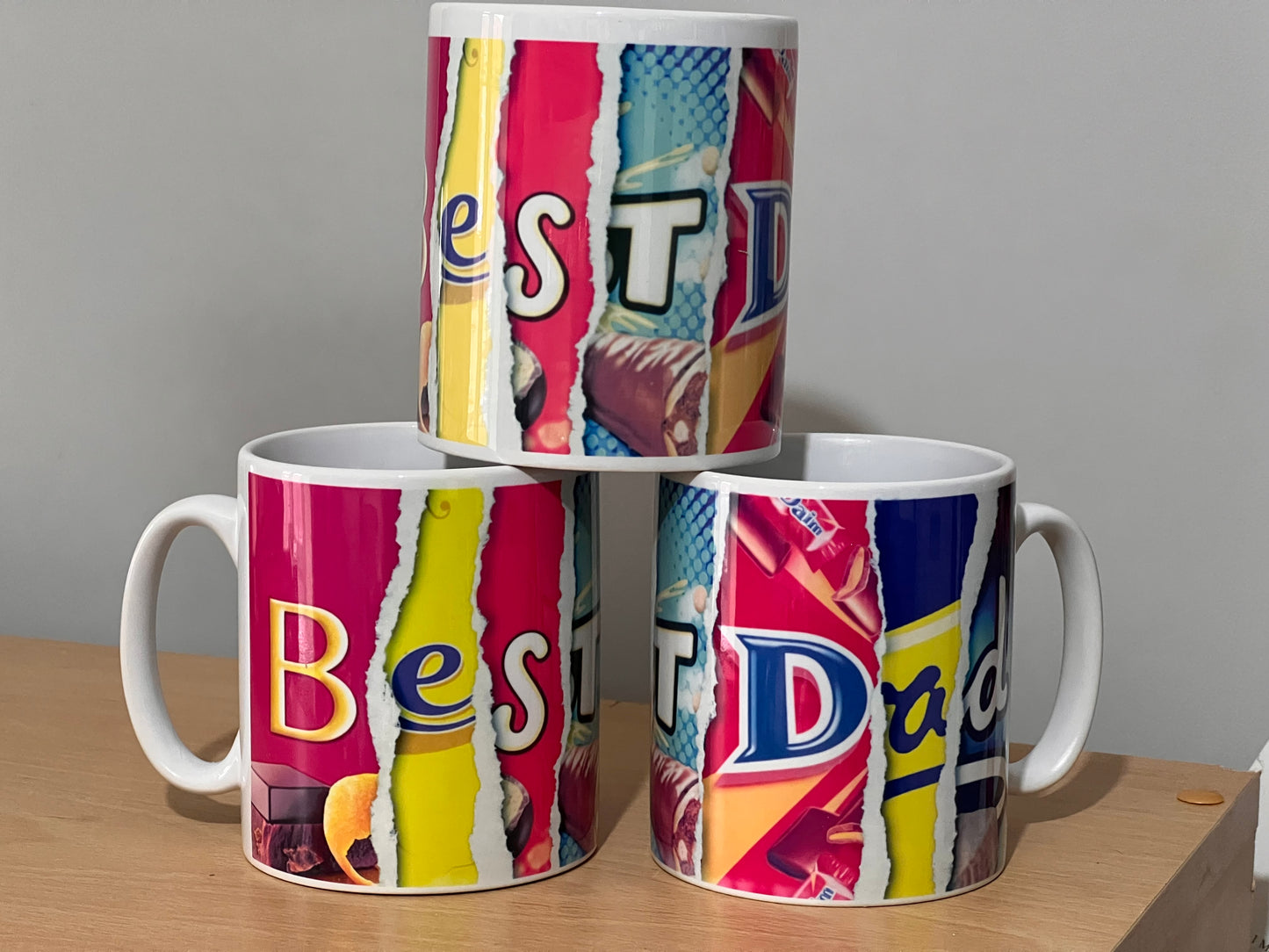 A stack of 3 mugs containing the words Best Dad which are formed using words from images from chocolate wrappers