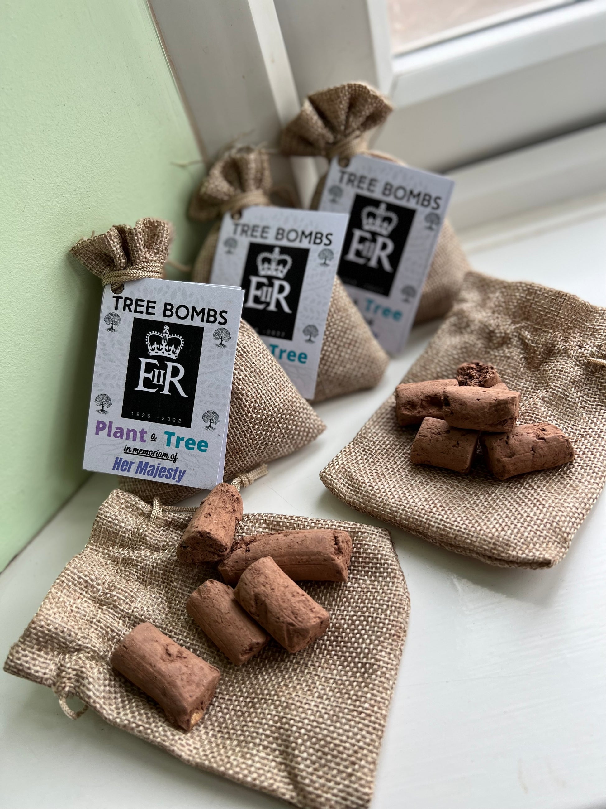 Burlap gift bag with Tree Bomb Label sitting beside another burlap gift bag showing the contents being seeds encased in a clay pellet shape